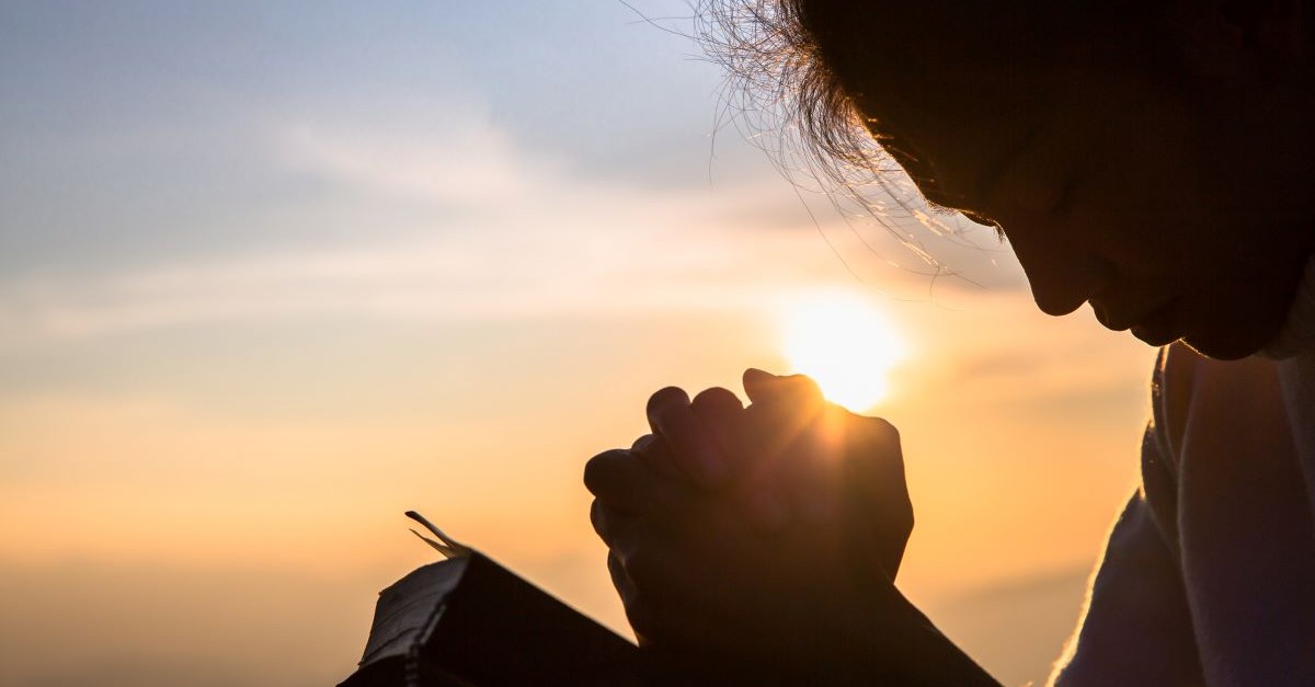 girl praying with bible head bowed sunset