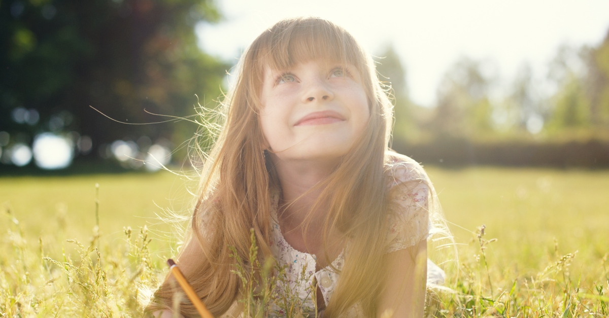 young girl lying in field writing looking up