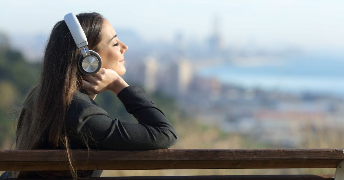 woman outside listening headphones city bench