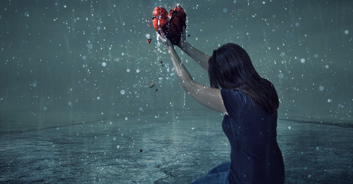 Woman holding a broken heart on her knees in the rain