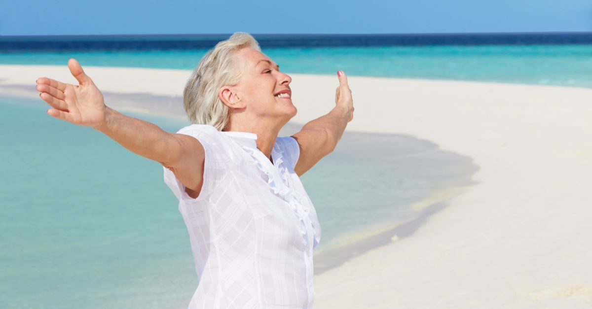 senior woman on beach arms out wide in joy