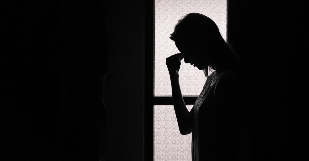 silhouette of woman in dark room looking distressed, prayer against attacks of enemy