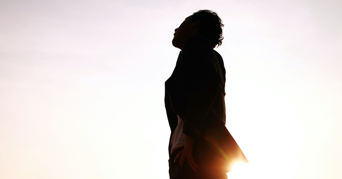 silhouette of man looking up and thinking outside in bright sky
