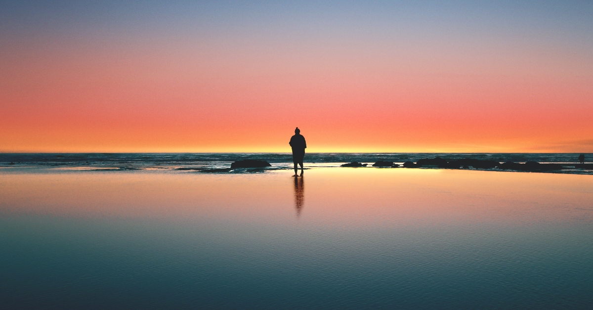man standing on shore at night under colorful sky alone, speaking in tongues