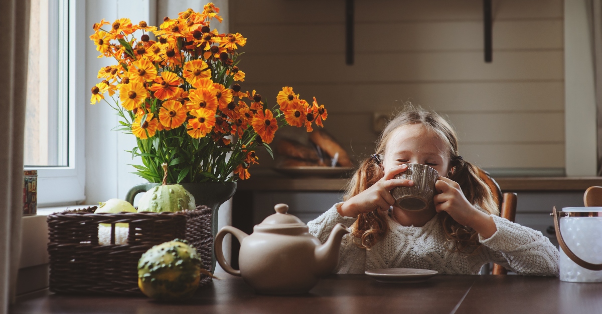 little girl with mug sitting at fall decorated table looking happy
