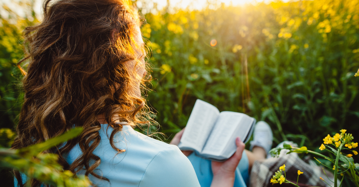 Woman in a sunny field reading the Bible