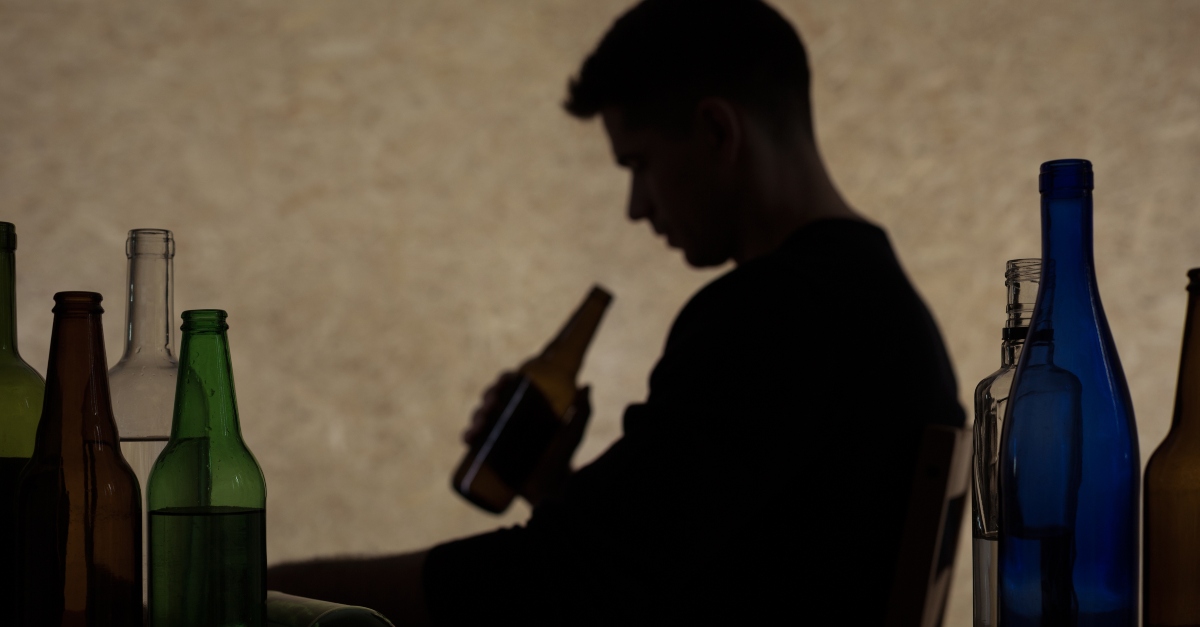 Worried man sitting among empty bottles of alcohol