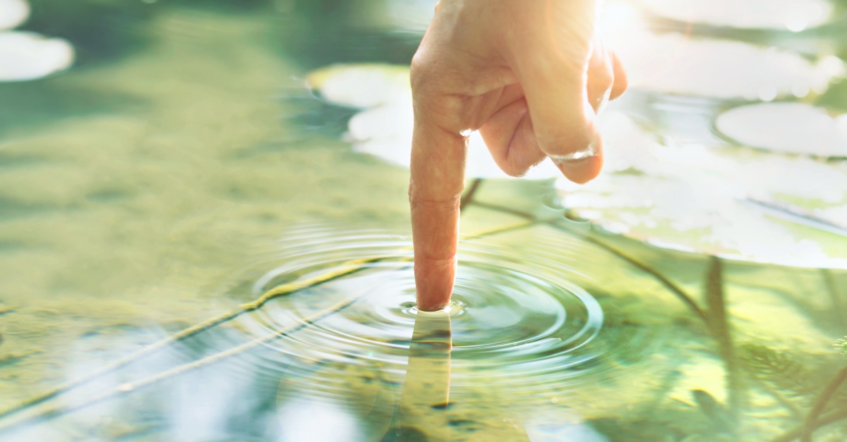 A finger touching the surface of the water making ripples