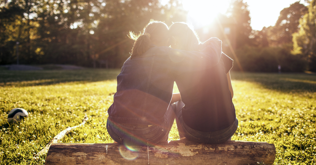 two friends consoling each other sitting on a log bench outside