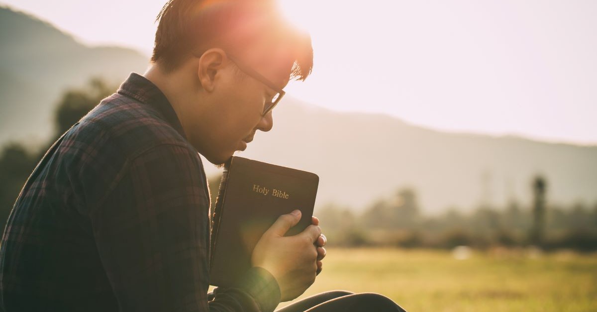 Man holding a Bible and praying at sunset