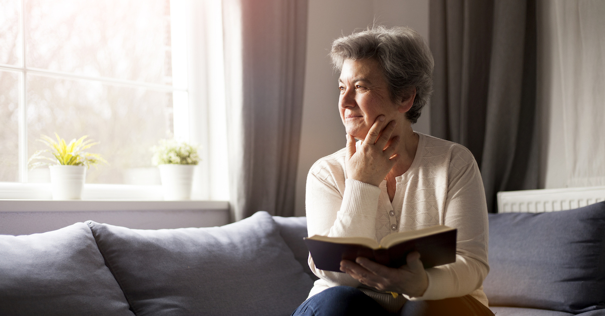 older woman sitting in living room with Bible thinking