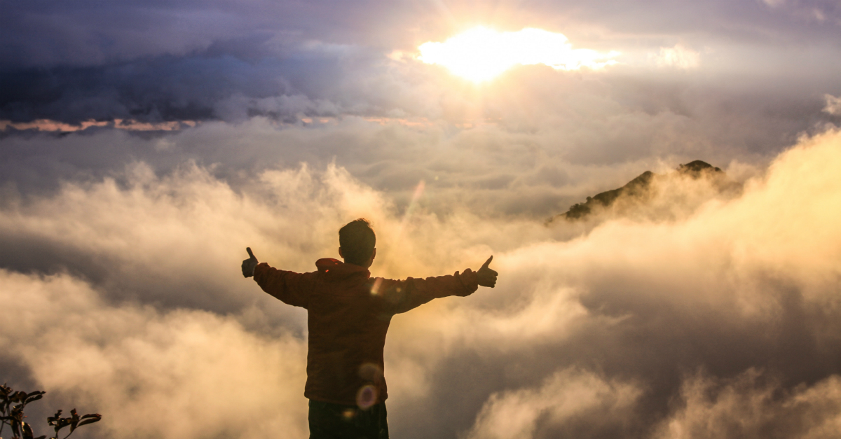 Man with thumbs up at the top of a mountain