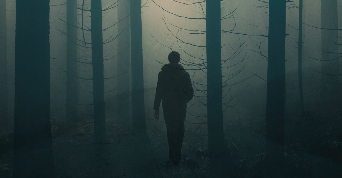 man walking through dark forest