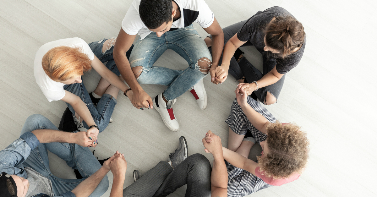 group of young people in a circle holding hands praying