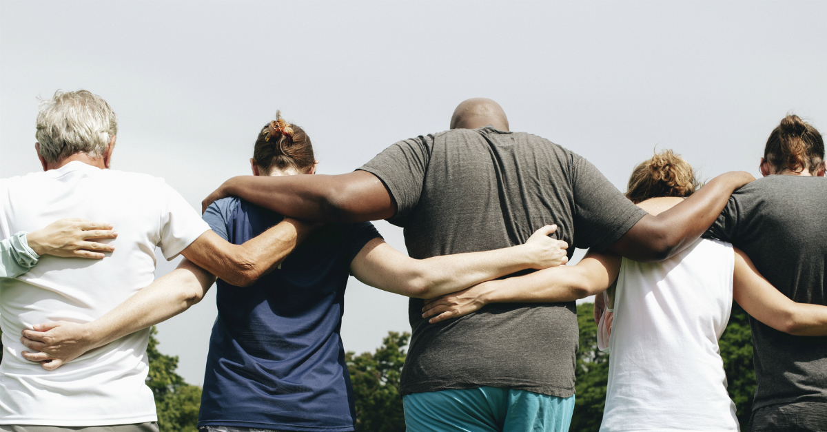 diverse row of group of adult friends with heads bowed in prayer arms around each other