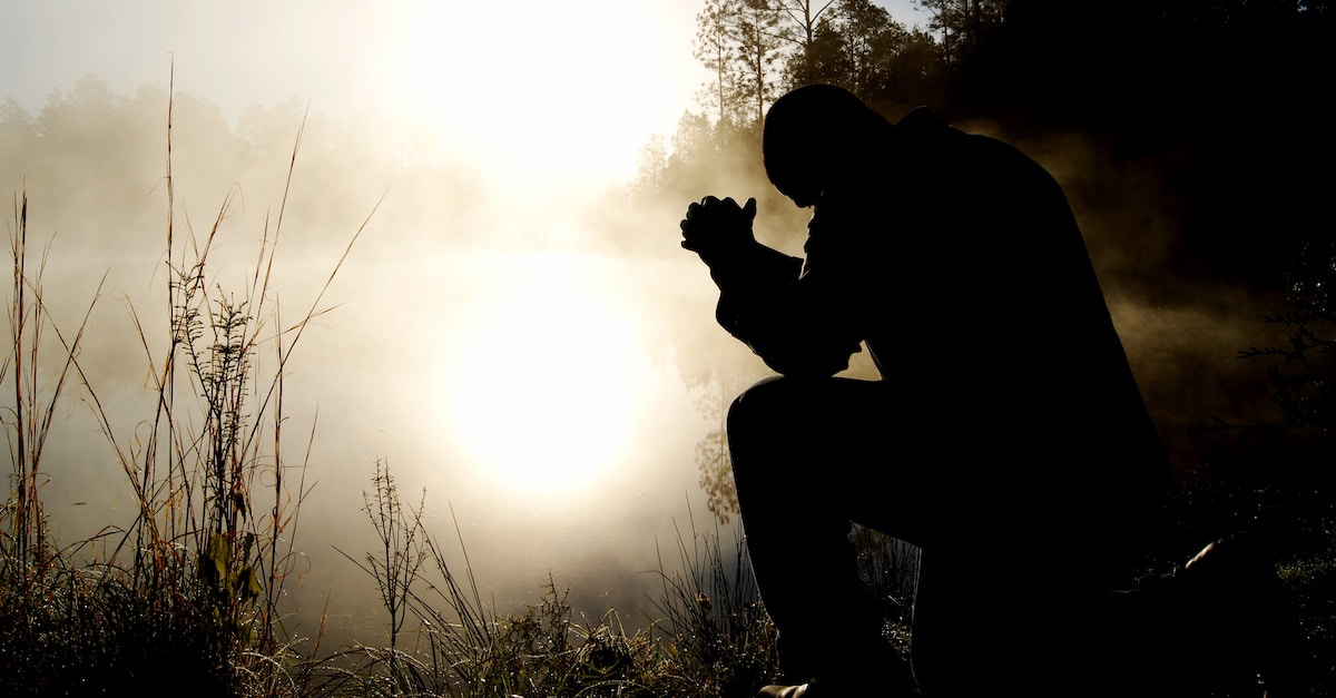 Silhouette of a man kneeling in prayer in the fog
