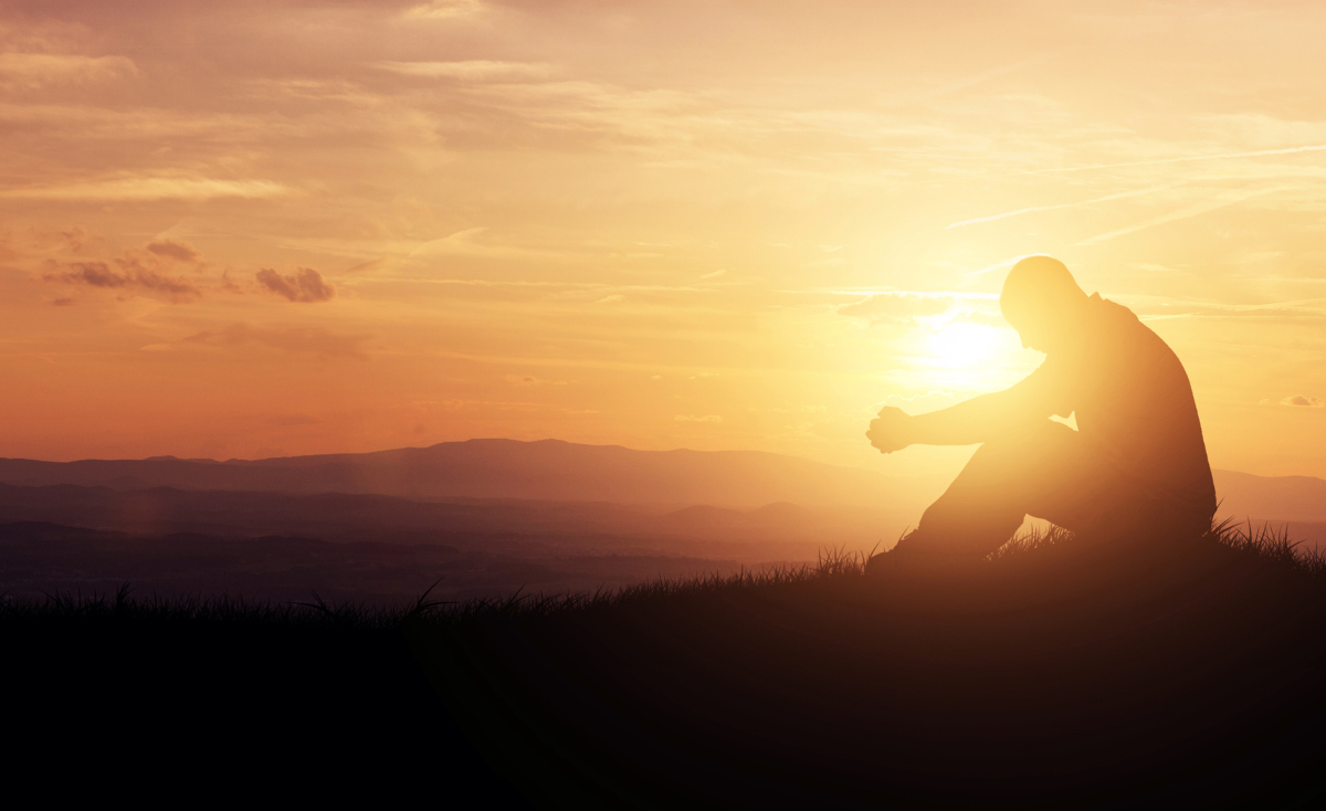 Man praying on a hill at sunset