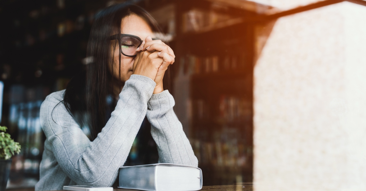 woman with glasses in coffee shop praying