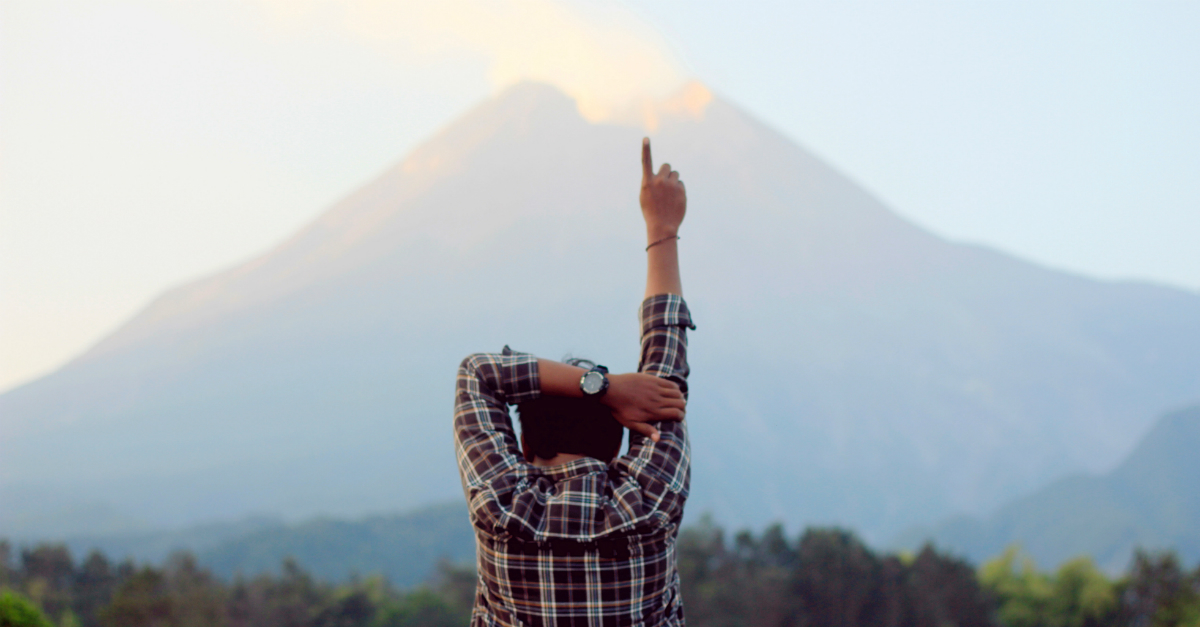 man pointing upward to God in praise outdoors with mountain in background