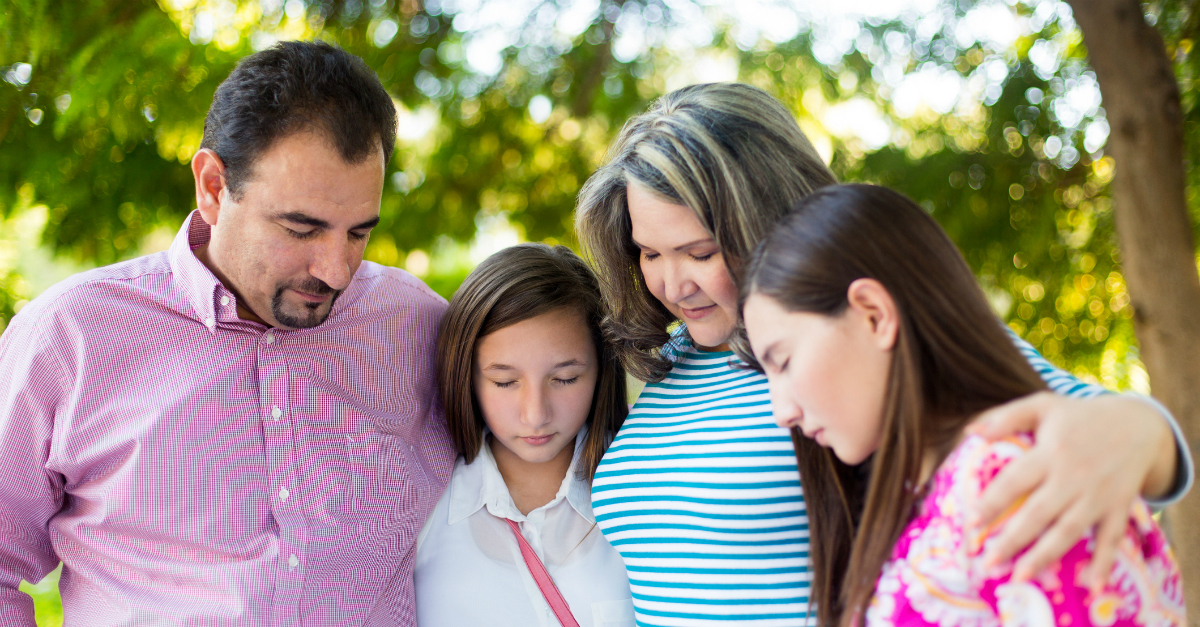 family of four outdoors group hug heads down in prayer together