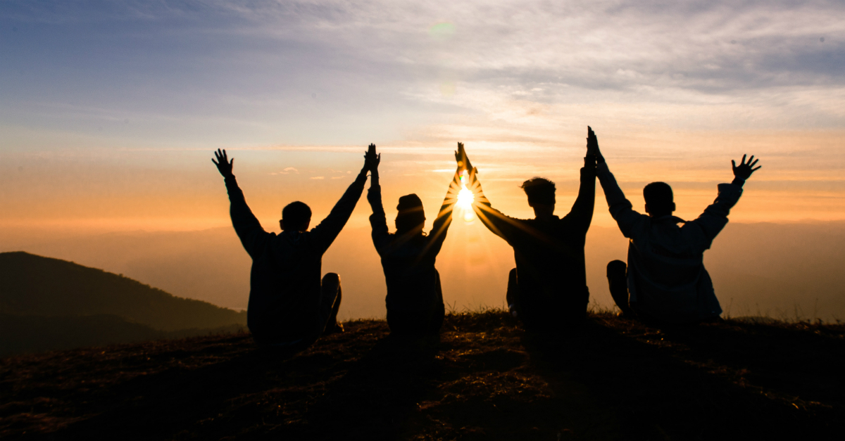 group of friends hands together arms up praising in wonder of sunset