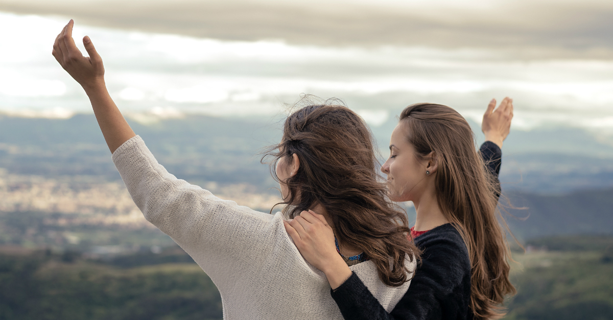 two young woman friends arms out in praise and prayer at scenic overlook