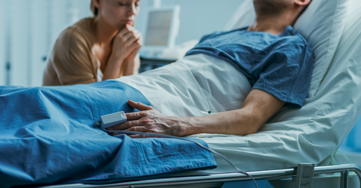 woman praying at hospitalized husband's bedside hoping God answers prayer