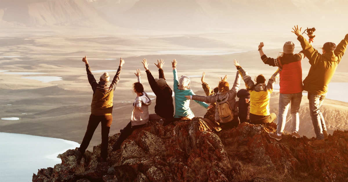 Group of hikers on a summit with arms raised in excitement