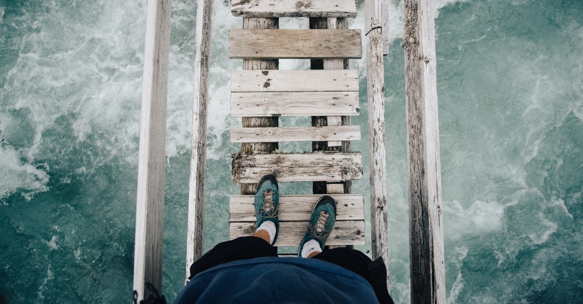 Person walking on a rickety bridge over rough water