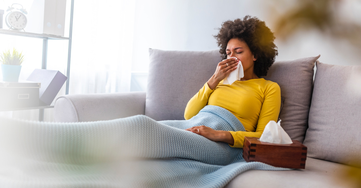 Sick woman lying on the couch, blowing her nose