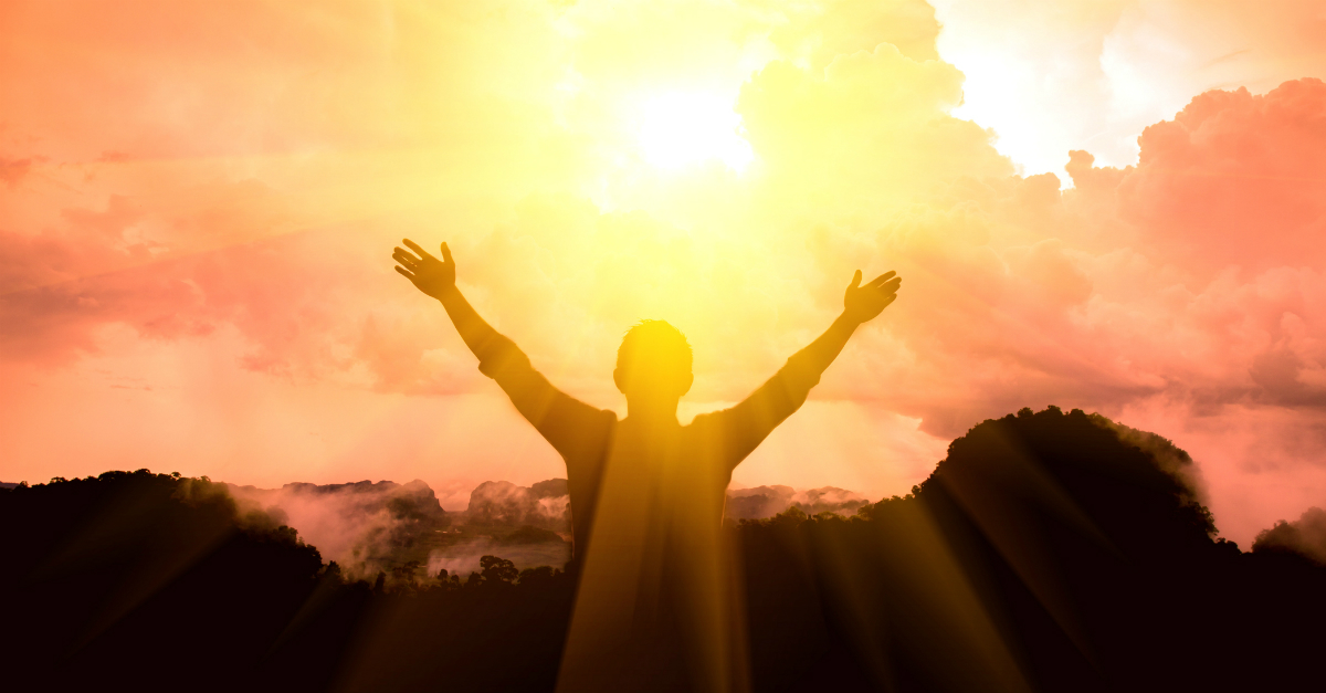 back view of person with arms up and out wide in praise at sunrise