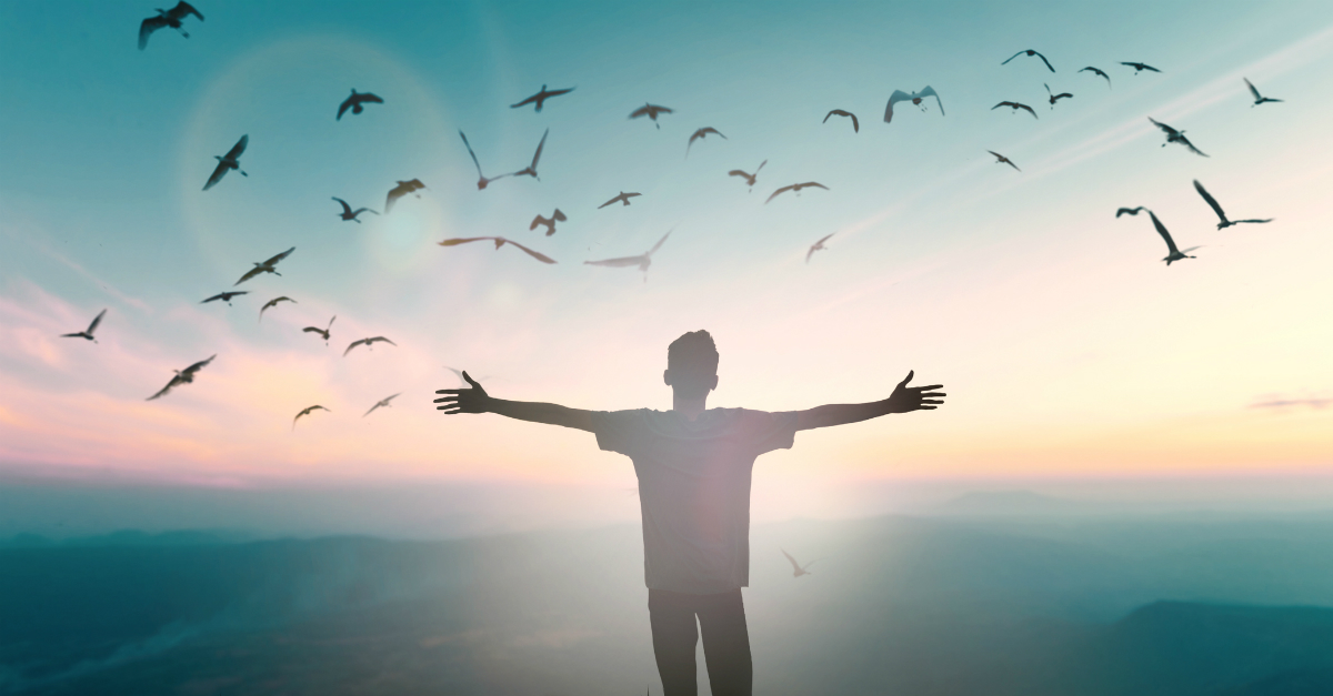 man with arms out wide in praise while birds in flight