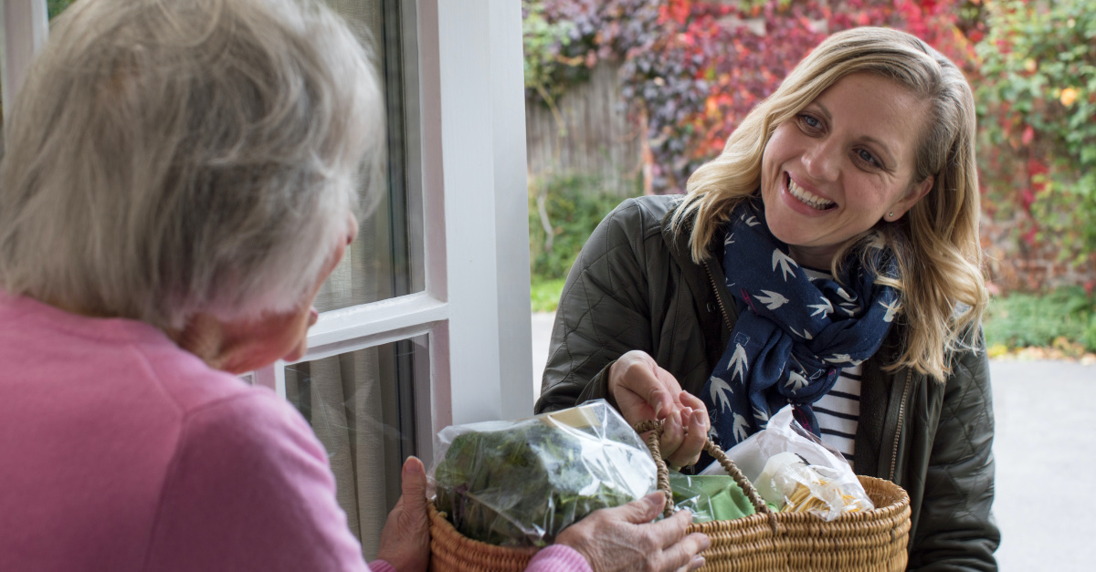 woman giving groceries to elderly woman joyfully