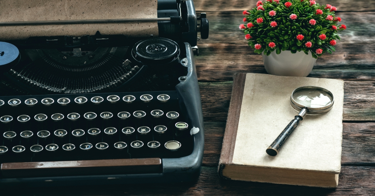 Typewriter on desk with book and magnifying glass and flowers