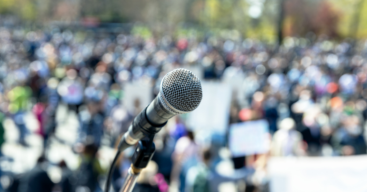 Microphone in front of a blurry crowd of people, at a rally