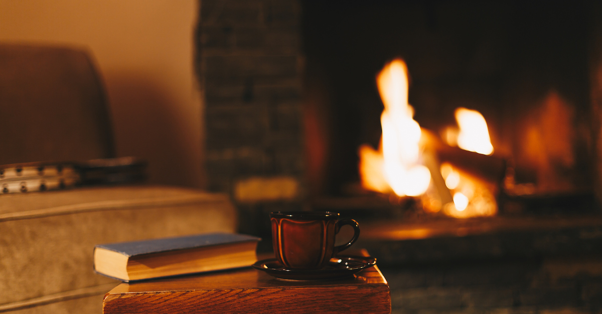 cozy fireplace with fire burning and book and mug nearby on stool