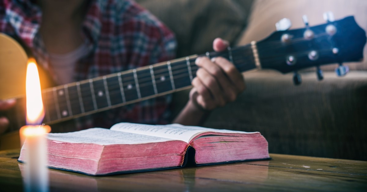 man playing guitar with bible and candle on coffee table, christian artists