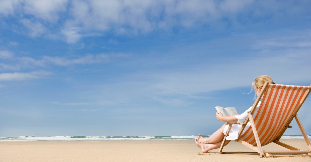 Woman sitting in a beach chair, reading by the ocean
