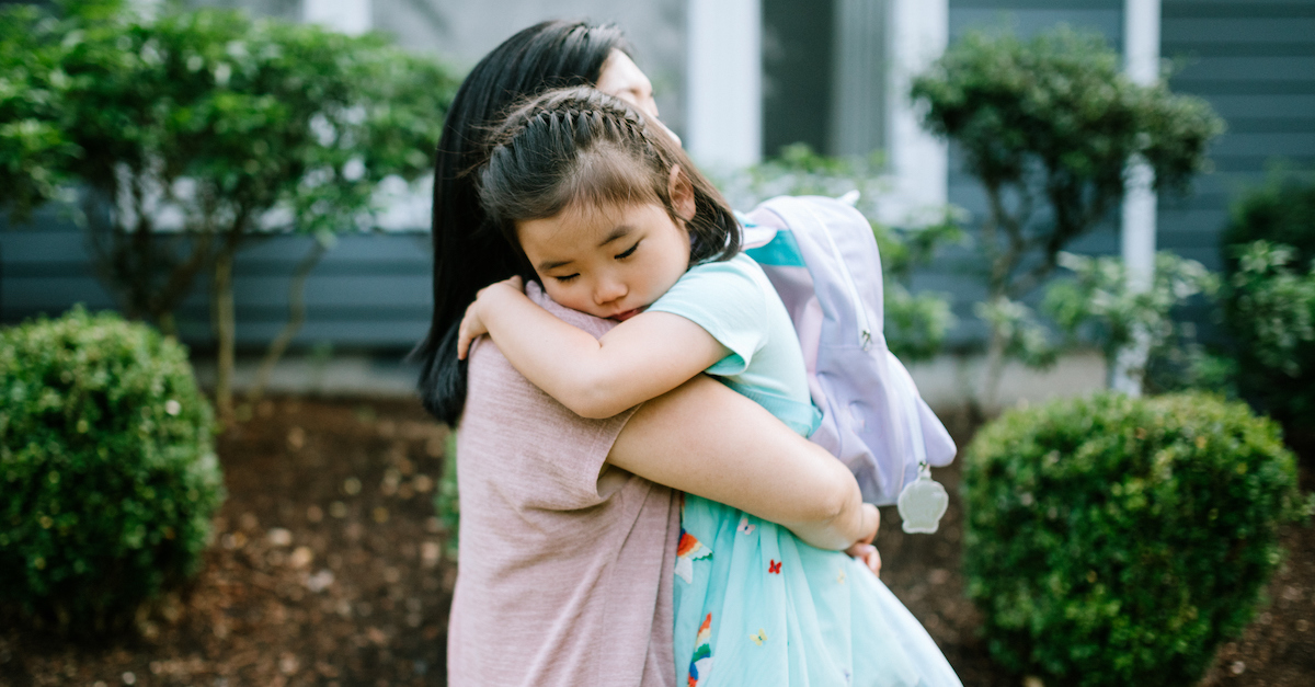 mom hugging daughter in backpack for school