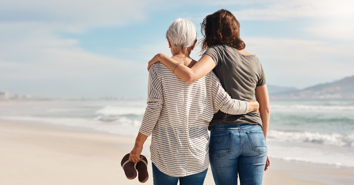 Older woman and younger woman walking arm in arm on the beach