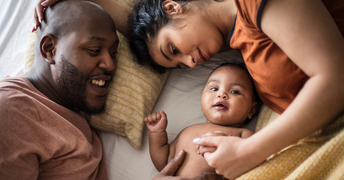 Family parents with newborn baby relaxing on bed