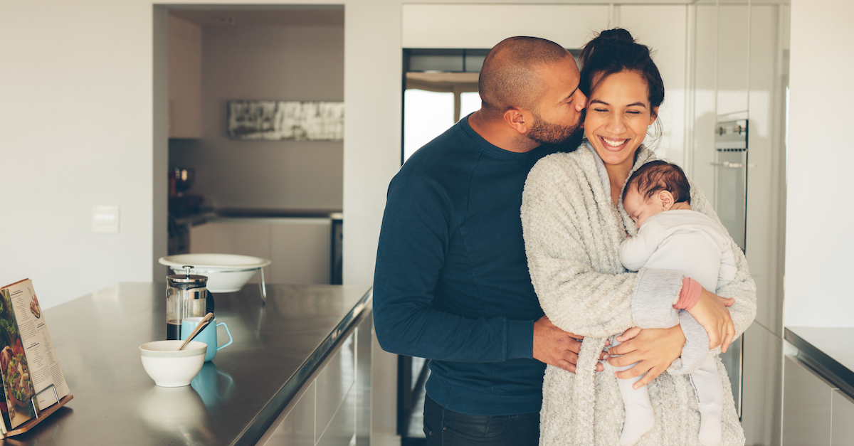Happy couple family parents in kitchen with baby kissing