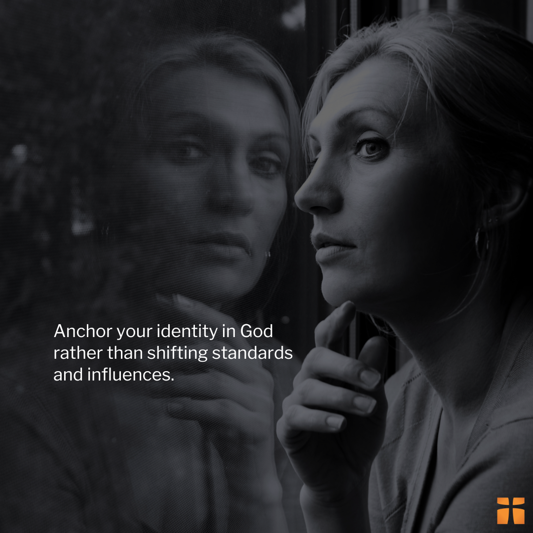 Black-and-white inspirational graphic showing a woman looking thoughtfully beside a reflective window, with her reflection visible in the glass. White text reads, “Anchor your identity in God rather than shifting standards and influences.” A small Christianity.com logo appears in the bottom corner.