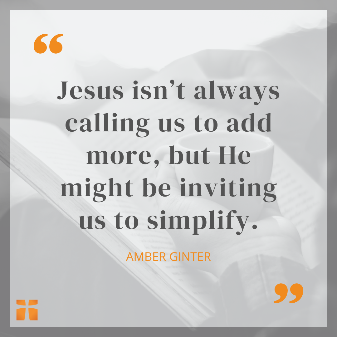 Quote graphic featuring a statement by Amber Ginter that reads, “Jesus isn’t always calling us to add more, but He might be inviting us to simplify,” displayed over a soft grayscale background of a person reading an open Bible while holding a cup of coffee.